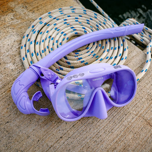 Purple diving mask and snorkel set on a concrete surface with rope in the background