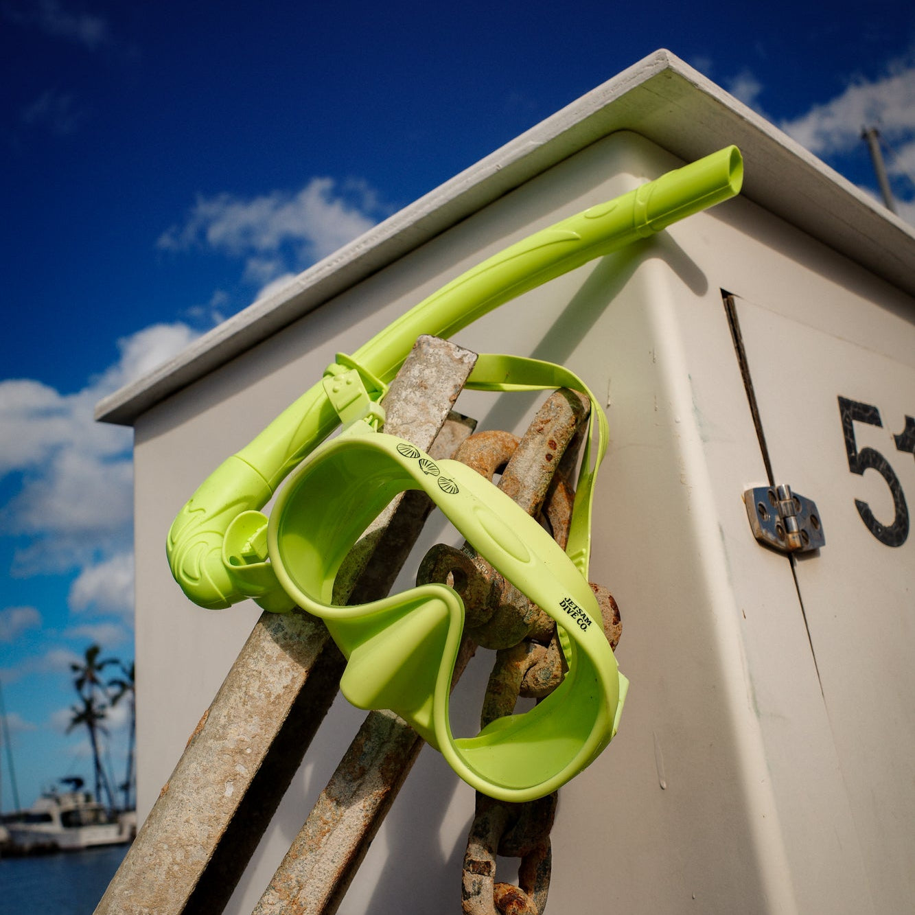 Neon green dive mask and snorkel on a anchor of a boat with a clear blue sky and water in the background