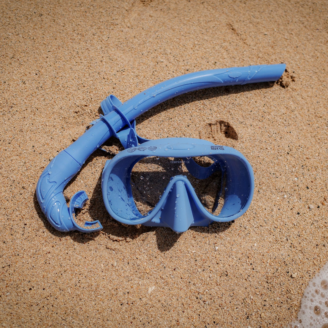 Blue snorkel and mask set on sandy beach with ocean water.