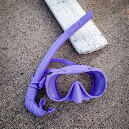 Purple diving mask and snorkel on a concrete surface
