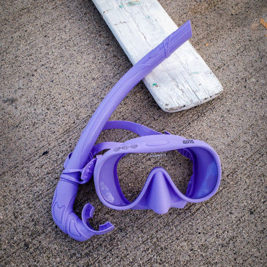 Purple diving mask and snorkel on a concrete surface